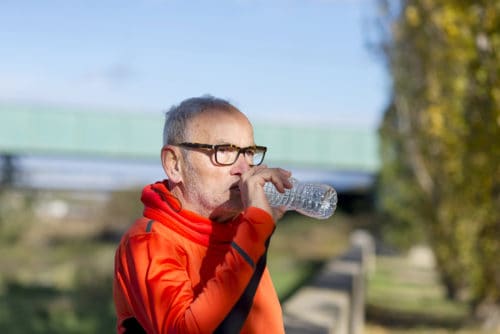 Handsome senior jogging man drinking fresh water from bottle aft