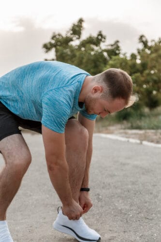 portrait of Caucasian guy in a blue t-shirt and black shorts,who ties his laces on white sports shoes before Jogging