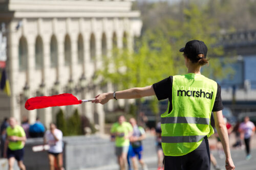 Volunteer holds a flag in his hand and points the way athletes runners